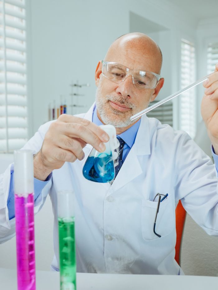 Scientist in a lab coat using pipette with colorful chemicals in a laboratory setting.