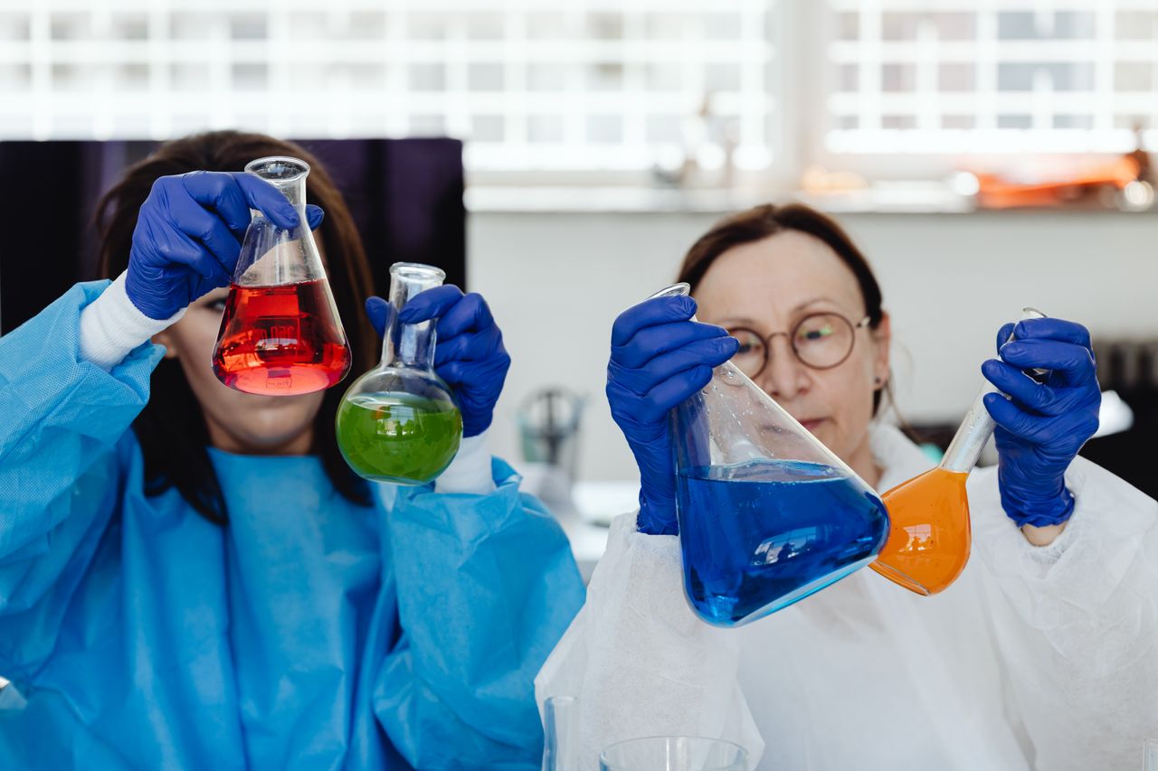 Two female scientists perform experiments with colorful chemicals in a lab environment.